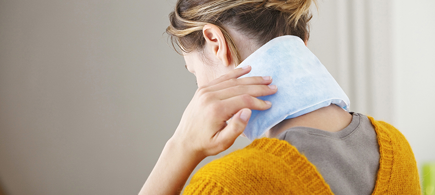 Photo of a womn using cold therapy for migraine headache relief. She is placing a cold pack over the carotid arteries in her neck.