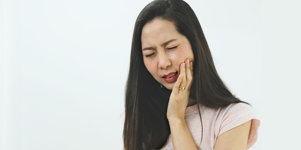 photograph of a woman holding her jaw due to TMJ pain and headache